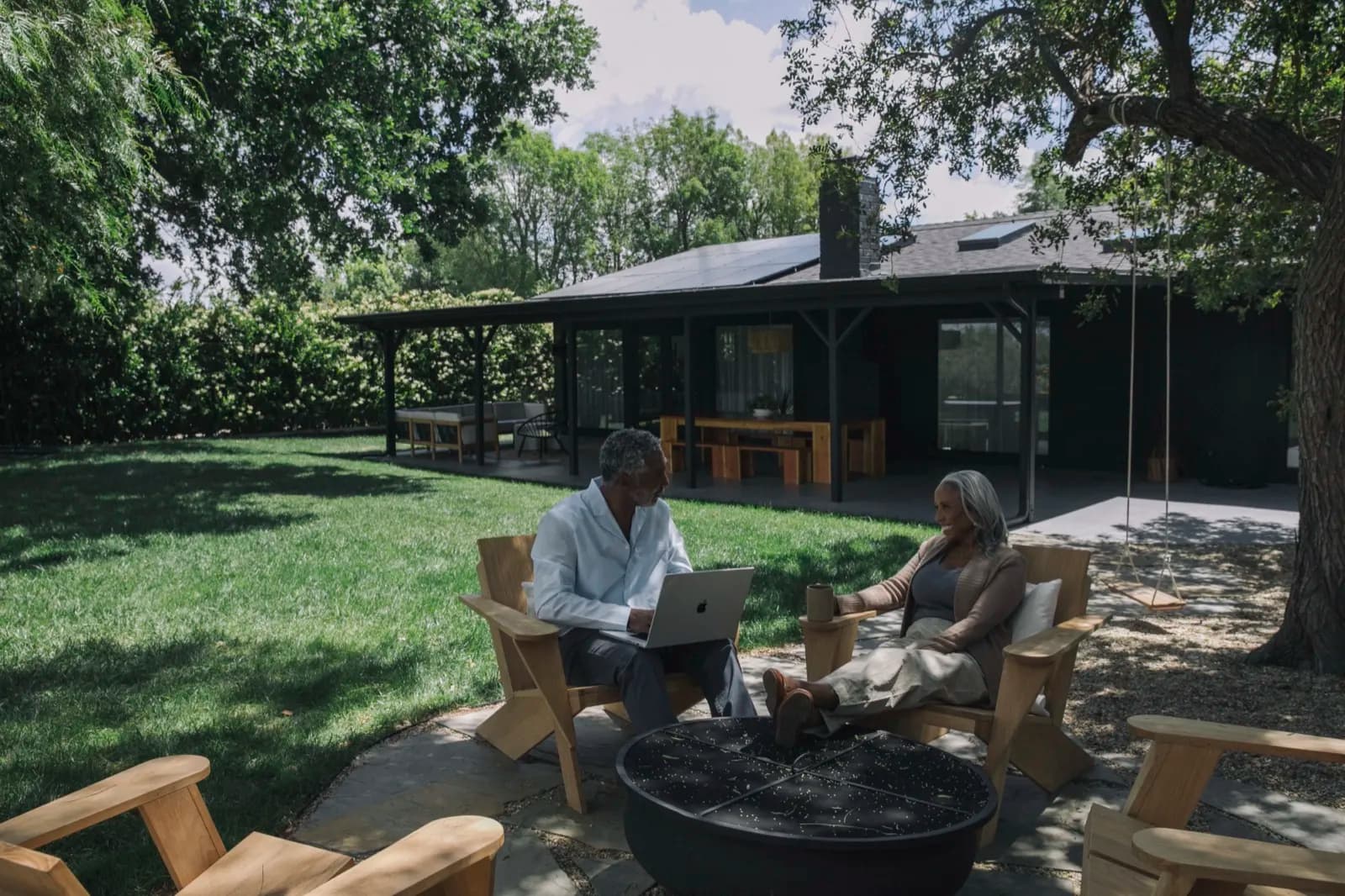 Couple relaxing in their backyard with a laptop, in front of their home with rooftop solar