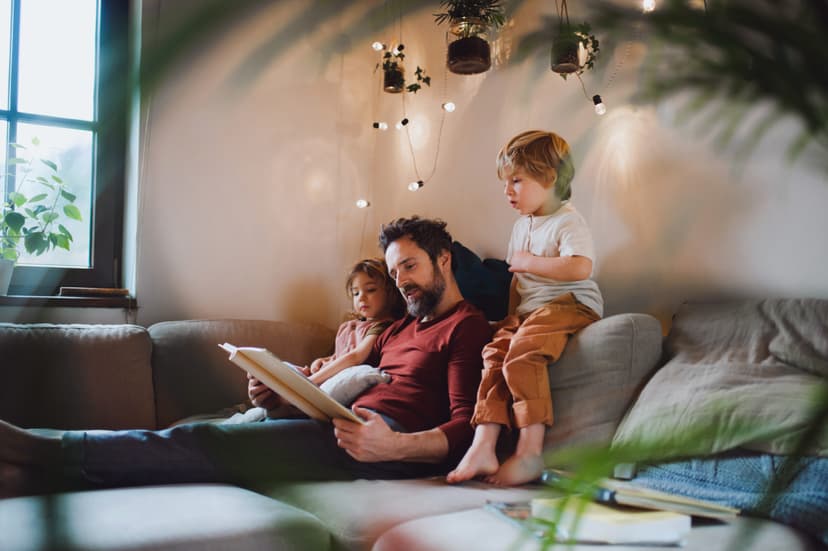 A father with two small children resting indoors at home, looking at photo album.