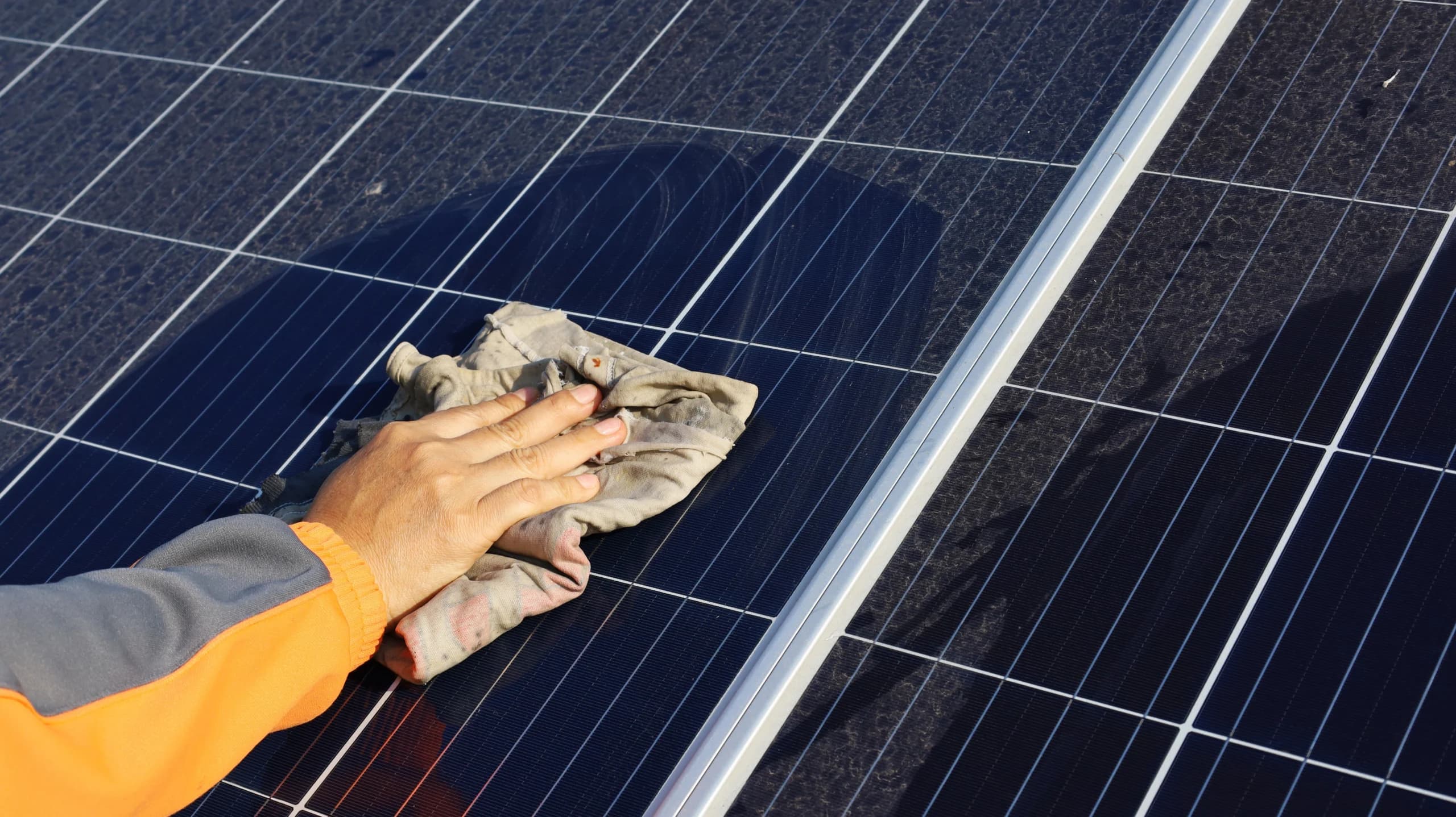 A person wipes dust off of a solar panel with a wet rag.